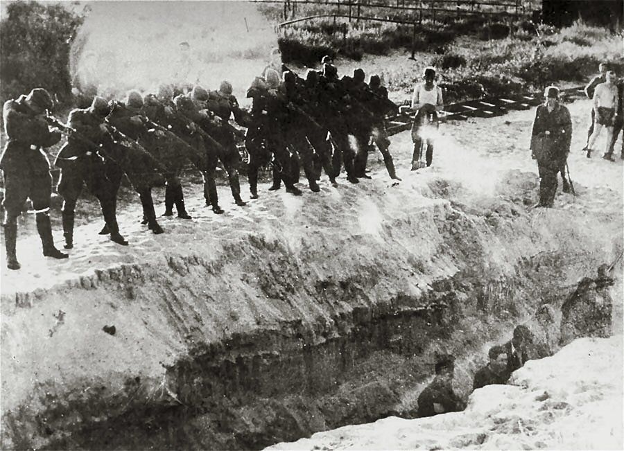 Members of an Einsatzkommando firing at men standing at the bottom of a trench. Circa : 1941-1942. Whereabouts unknown. Photographer unknown.